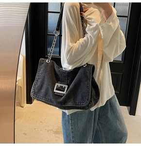 Detail of dark washed denim tote bag with silver metal buckle and chain shoulder strap