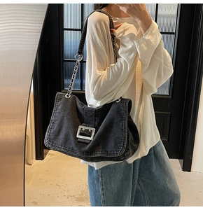 Detail of black denim tote bag with silver buckle and chain strap on a female model