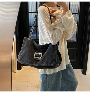 Detail of black denim shoulder bag with silver chain strap and metal buckle on model