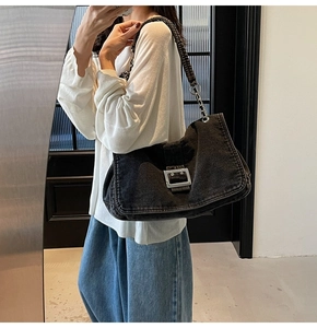 Detail of black denim shoulder bag with large silver buckle and metal chain strap