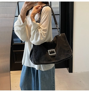 Detail of a black denim shoulder bag featuring a large silver square metal buckle and chain strap