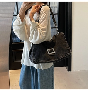 Detail of black denim shoulder bag featuring a large silver buckle and chain strap