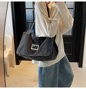 Detail of denim shoulder bag featuring a silver metal buckle and chain strap