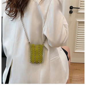 Detail of green woven mini crossbody bag with metal chain strap on white blazer