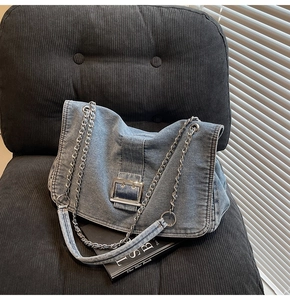 Detail of blue denim tote bag with silver square buckle and chain strap on grey chair
