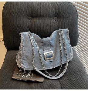 Close-up of blue denim chain tote bag with silver metal buckle on grey textured seat