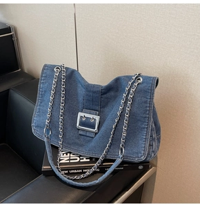 Detail of denim tote bag with silver buckle and chain strap on black leather chair