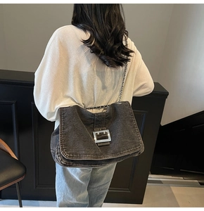 Detail of grey denim crossbody bag with thick silver chain and square metal buckle