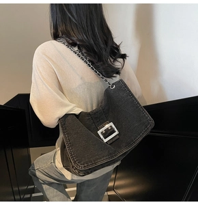 Rear view of model wearing a large black denim tote bag with silver metal buckle and chain