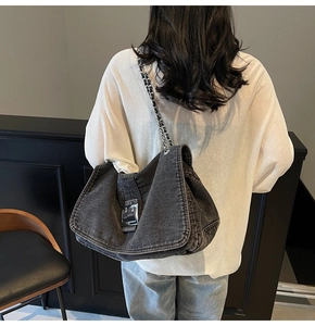 Detail of grey denim tote bag featuring silver chain strap and metal buckle on a model