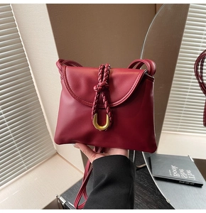 Detail of burgundy leather shoulder bag with woven knot and golden metal U-shaped buckle