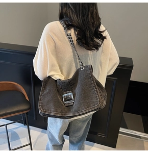 Detail of grey denim shoulder bag with bold silver buckle and chain strap on a model