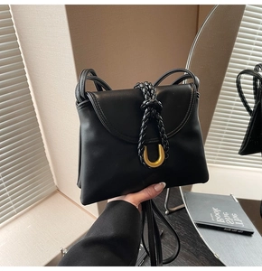 Detail view of black matte leather bag featuring a gold U-shaped buckle and woven strap design