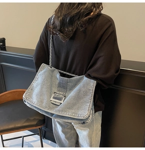 Detail of blue denim tote bag with silver chain strap and metal buckle worn by model
