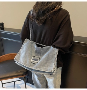 Detail of blue denim tote bag with silver chain strap and metal buckle on model back