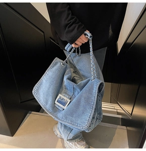 Detail of light blue denim tote bag with silver metal buckle and chain strap shown on model