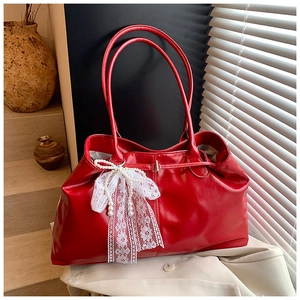 Detail of red glossy leather tote bag featuring a white lace and pearl bow charm