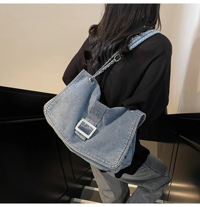 Blue denim tote bag with woven metal chain strap and silver buckle detail on shoulder