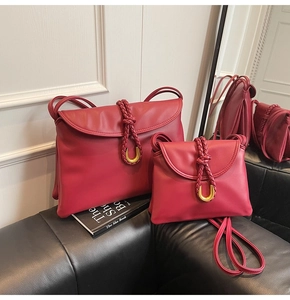 Detail of two burgundy leather envelope bags with braided gold buckles on a black sofa
