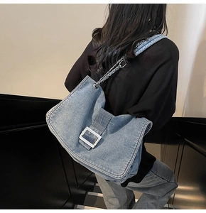 Detail of blue denim shoulder bag featuring silver metal buckle and chain strap on model