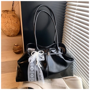 Close-up of black glossy oil wax leather tote bag with lace bow and pearl charm detail