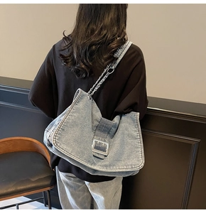 Macro shot of large denim tote bag featuring oversized silver buckle and chain shoulder strap