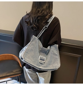 Detail of blue denim tote bag featuring silver metal buckle and chain shoulder strap