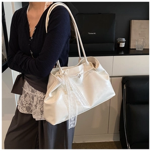Close-up of white tote bag featuring lace bow and pearl chain accents on glossy leather