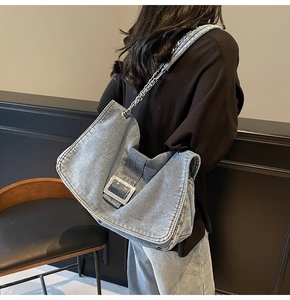 Detail of light blue denim hobo bag featuring a large silver buckle and chain strap