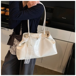 Detail of a creamy white leather tote bag featuring a lace bow and pearl tassel accents