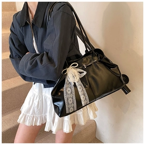 Detail of black leather tote bag featuring a white lace bow and pearl charm ornament