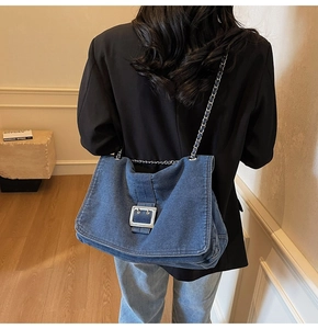 Close-up of blue denim tote bag with silver chain strap and metal buckle on the model
