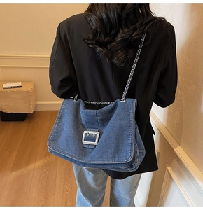 Detail of large denim tote bag with silver chain strap and metal buckle on woman shoulder