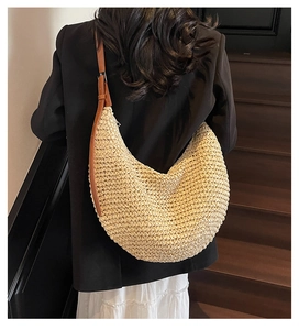 Straw hobo bag with brown leather strap worn by model over a black blazer and white skirt