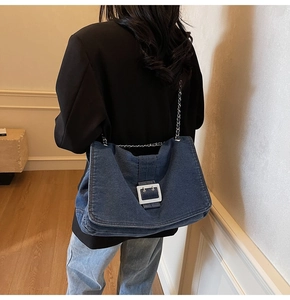 Detail of blue denim tote bag featuring silver chain strap and white resin buckle