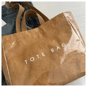 Detail of waterproof brown tote bag showing glossy texture and white TOTE BAG text