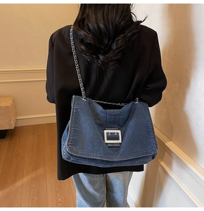 Detail of blue denim tote bag with silver square buckle and chain strap on person