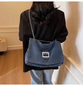 Detail of a large dark blue denim tote bag with silver chain strap and metal buckle