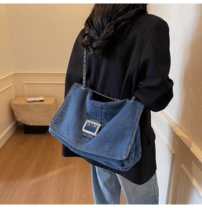 Detail of blue denim tote bag with silver metal buckle and chain strap shown on model