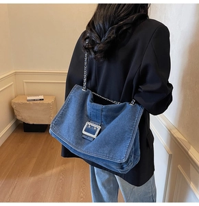 Detail of blue denim tote bag with silver metal buckle and chain strap on shoulder