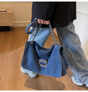 Detail of blue denim tote bag featuring a metallic square buckle and chain strap style