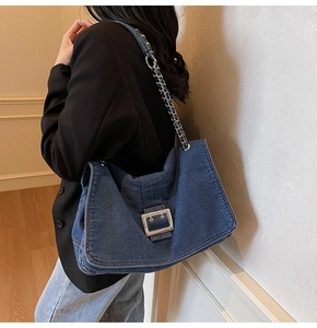 Detail of blue denim tote bag with large silver buckle and metal chain strap on model