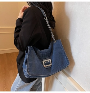 Detail view of large denim shoulder bag with silver buckle and metal chain strap