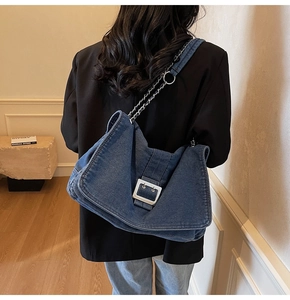 Detail of blue denim tote bag with silver chain strap and metal buckle on the shoulder