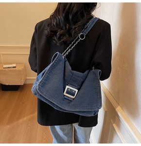 Detail of blue denim tote bag with silver buckle and chain strap on a model