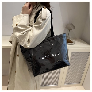 Chic black glossy tote bag with white TOTE BAG text shown on a fashion model's shoulder