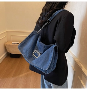 Detail of blue denim tote bag featuring large silver buckle and metal chain shoulder strap