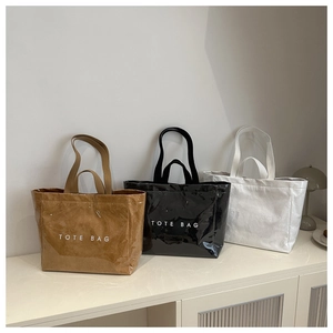 Three glossy tote bags in tan black and white colors with minimalist letters on cabinet