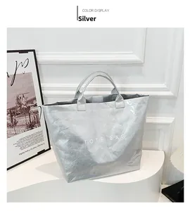 Modern silver Tyvek tote bag featuring bold white text displayed in a minimalist studio