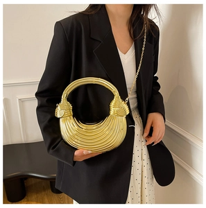 Detail of a gold crescent-shaped metal handbag with textured horizontal stripes and chain